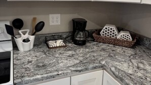 A kitchen with white cabinets, a granite countertop, a coffee maker, and kitchen utensils. - Cozy West Duplex (Seymour)