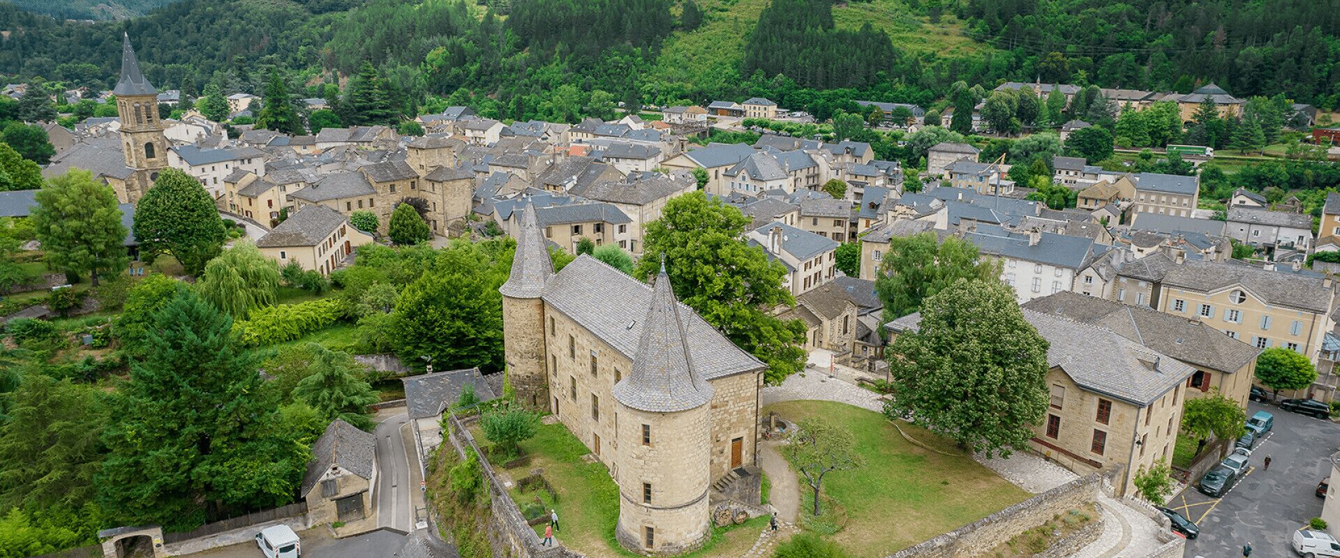 An aerial view of a historic town with stone buildings, a prominent tower, and lush greenery.