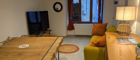 Una sala de estar con una mesa de comedor de madera, un sofá, un televisor y una ventana con cortinas.