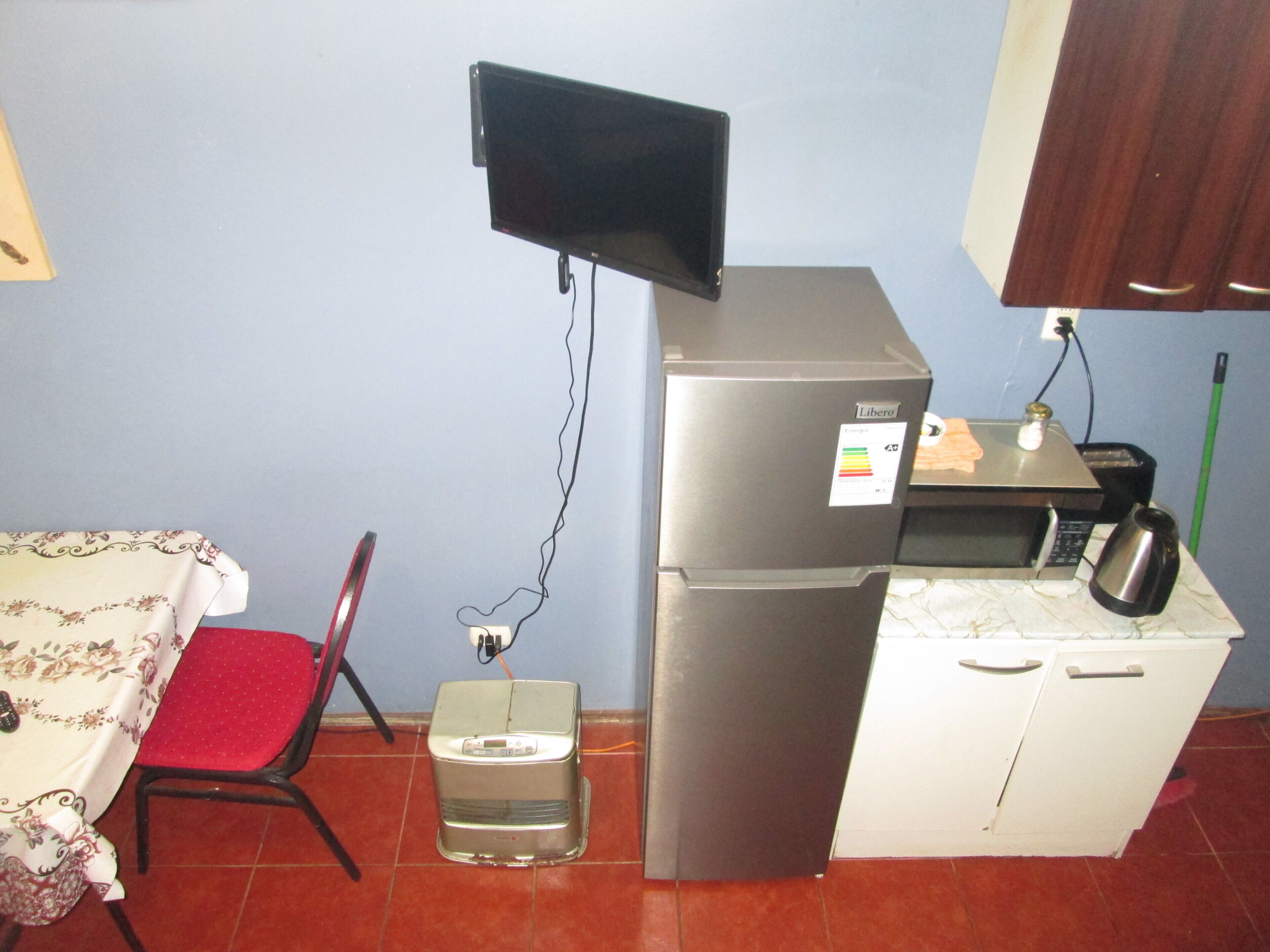 A compact kitchen with a refrigerator, a toaster, a microwave, and a small table with a chair.