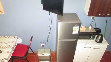 A compact kitchen with a refrigerator, a toaster, a microwave, and a small table with a chair.