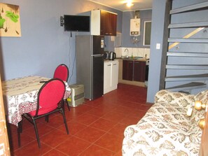 A compact kitchen with a refrigerator, microwave, and a small sink. There is a dining table with chairs and a sofa in the living area. - C3 Furnished Cabin Close to downtown Puerto Montt (Coyhaique)
