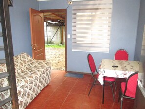 A room with a patterned sofa, a dining table with red chairs, and a window with blinds. - C3 Furnished Cabin Close to downtown Puerto Montt (Coyhaique)