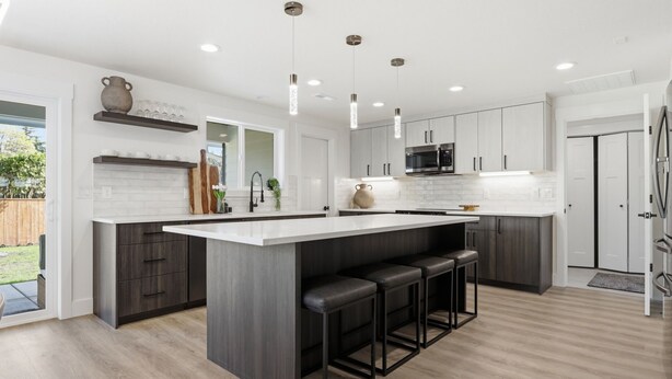 A modern kitchen with a large island, bar stools, pendant lighting, and a view of the backyard. - Modern, fully updated 4-BR house in cul-de-sac (Vancouver)