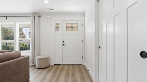 A room with a wooden floor, a beige sofa, a white door with a window, and a small round ottoman. - Modern, fully updated 4-BR house in cul-de-sac (Vancouver)