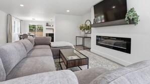 A modern living room with a sectional sofa, a glass coffee table, a flat-screen TV mounted on the wall, and a fireplace. - Modern, fully updated 4-BR house in cul-de-sac (Vancouver)