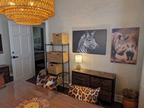 A dining area with a wooden table, patterned cushions, wicker baskets, and wall art of a zebra and rhino. - Safari House (Indianapolis)