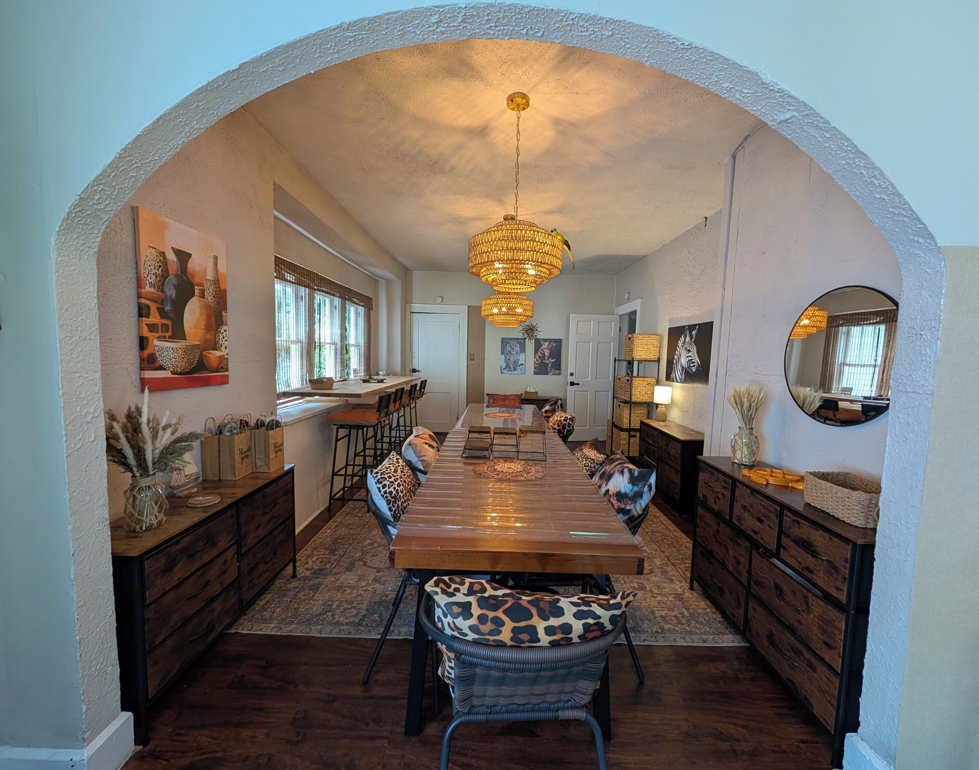 A dining area with a long wooden table, chairs with leopard print cushions, a chandelier, and a large mirror on the wall.. Safari House