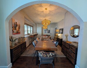 Un espace repas avec une longue table en bois, des chaises dotées de coussins à motifs léopard, un lustre et un grand miroir au mur.