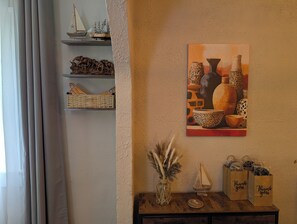 Una habitación con un estante de madera que alberga objetos decorativos, un cuadro colgado en la pared, un florero con plumas y una maqueta de un pequeño velero.