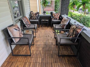 A covered outdoor seating area with a wooden floor, black metal chairs with cushions, and a central table. - Safari House (Indianapolis)