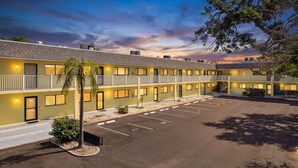 Un motel con estructura de dos pisos, un estacionamiento y un árbol en primer plano.