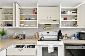 Une cuisine avec des meubles blancs, une cuisinière, un four à micro-ondes et divers ustensiles de cuisine.