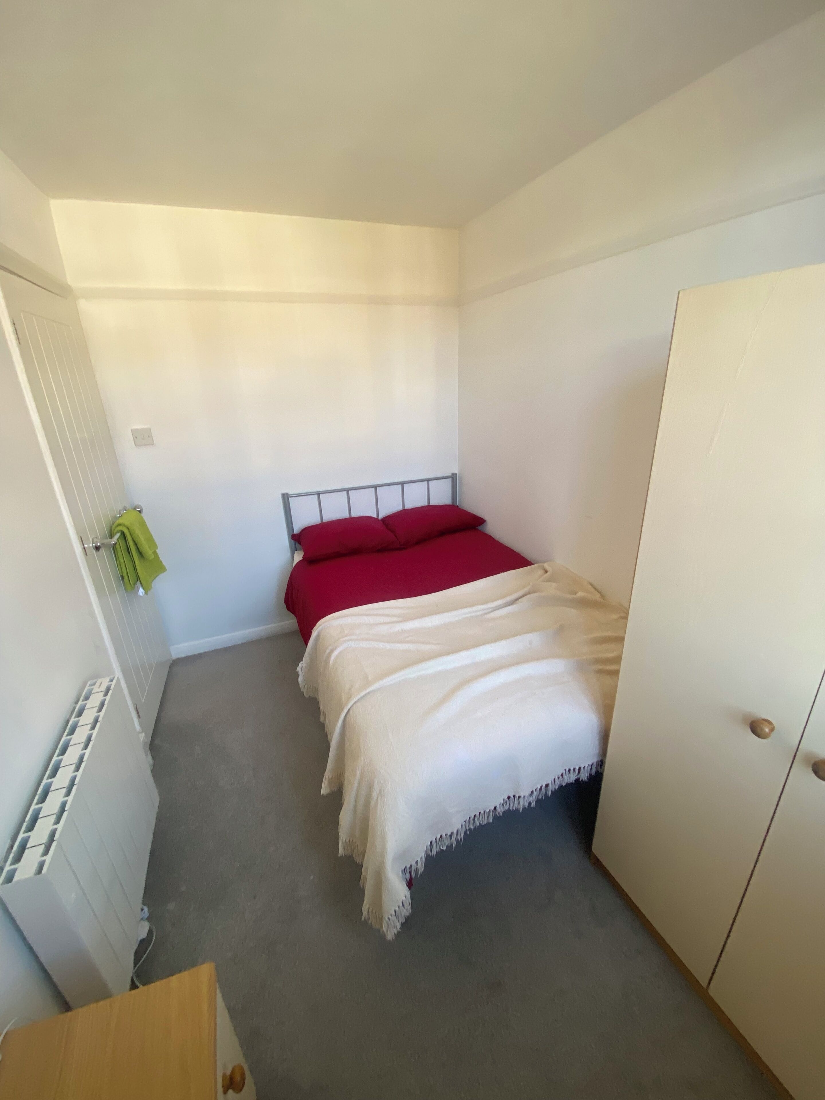 A small, single-bed room with a radiator, a wardrobe, and a green towel on the radiator.