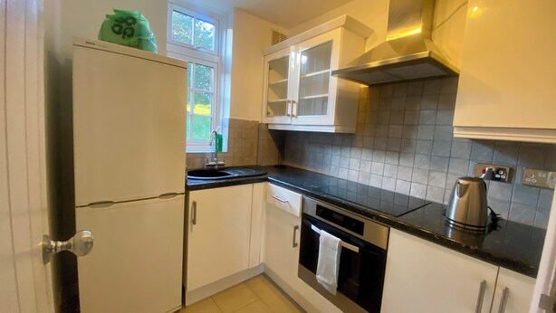 A modern kitchen with white cabinets, a stainless steel oven, a black countertop, and a window with a view of greenery.