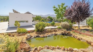 A modern building with a rooftop pool, surrounded by a landscaped garden with a small pond and various plants. - La Carraca Archidona by Ruralidays (Málaga)