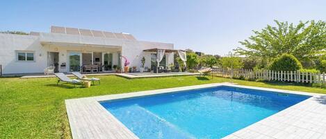 Une maison moderne dotée d’une piscine, d’un patio avec des chaises longues et d’un jardin.