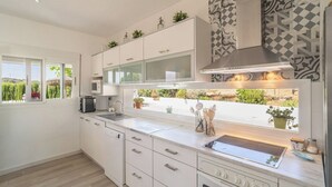 Ett modernt kök med vita skåp, en inbyggd ugn och ett fönster med utsikt över grönområden.