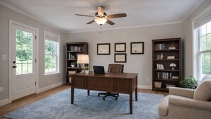 Ein Home-Office mit Schreibtisch, Stuhl, Bücherregal und Deckenventilator.