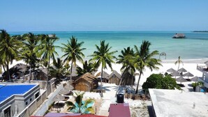 A beach resort with thatched-roof huts, palm trees, and a clear view of the ocean. - Zanzibar holiday villa (Zanzibar)