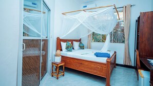 A bedroom with a wooden bed, a small bedside table, a window with a view, and a mosquito net over the bed. - Zanzibar holiday villa (Zanzibar)