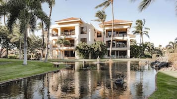 A two-story building with balconies, surrounded by palm trees and a water feature.