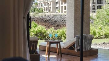 A sun lounger, a small round table with two glasses, and a view of a resort area with buildings and greenery.