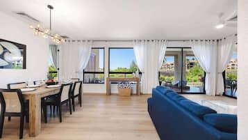 A modern living room with a dining area, large windows, and a blue sofa.