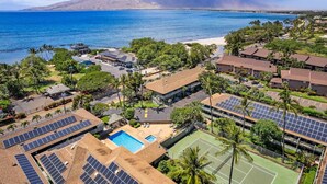 Un resort con paneles solares, piscina, cancha de tenis y vistas al océano.