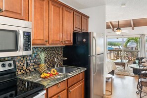 A kitchen with wooden cabinets, a microwave, a stove, and a refrigerator. - Ocean View Escape | Lanai, Pool & Maui Sunsets (Kihei)