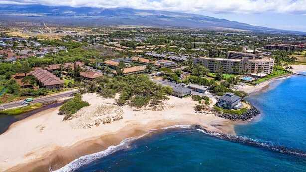 Vista aérea de un complejo turístico costero con propiedades frente a la playa, un gran hotel y una carretera que recorre la playa.