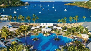 Ett semesterparadis med en pool i mitten, palmer och båtar i bakgrunden.