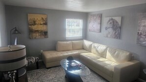 En stue med en beige sofa, et glasbord og billedkunst på væggene.