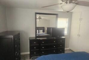 Een slaapkamer met een bed, een dressoir, een televisie, een plafondventilator en een kledingkast.