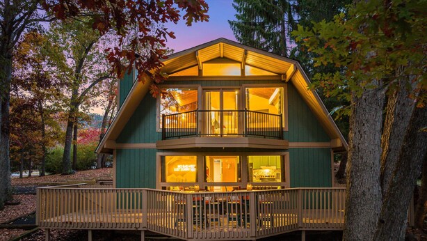 Une cabane à deux étages avec un balcon, entourée d’arbres et dotée d’une terrasse en bois.