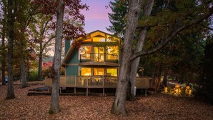 Une cabane à deux étages avec une terrasse, entourée d’arbres et recouverte de feuilles mortes.