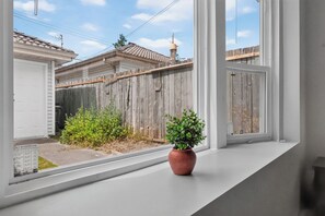 A window with a view of a wooden fence, a potted plant, and a clear sky. - Spacious 2BR Ground-Level Suite Near Kingsway Central Park & Metrotown 🌿 (Vancouver)