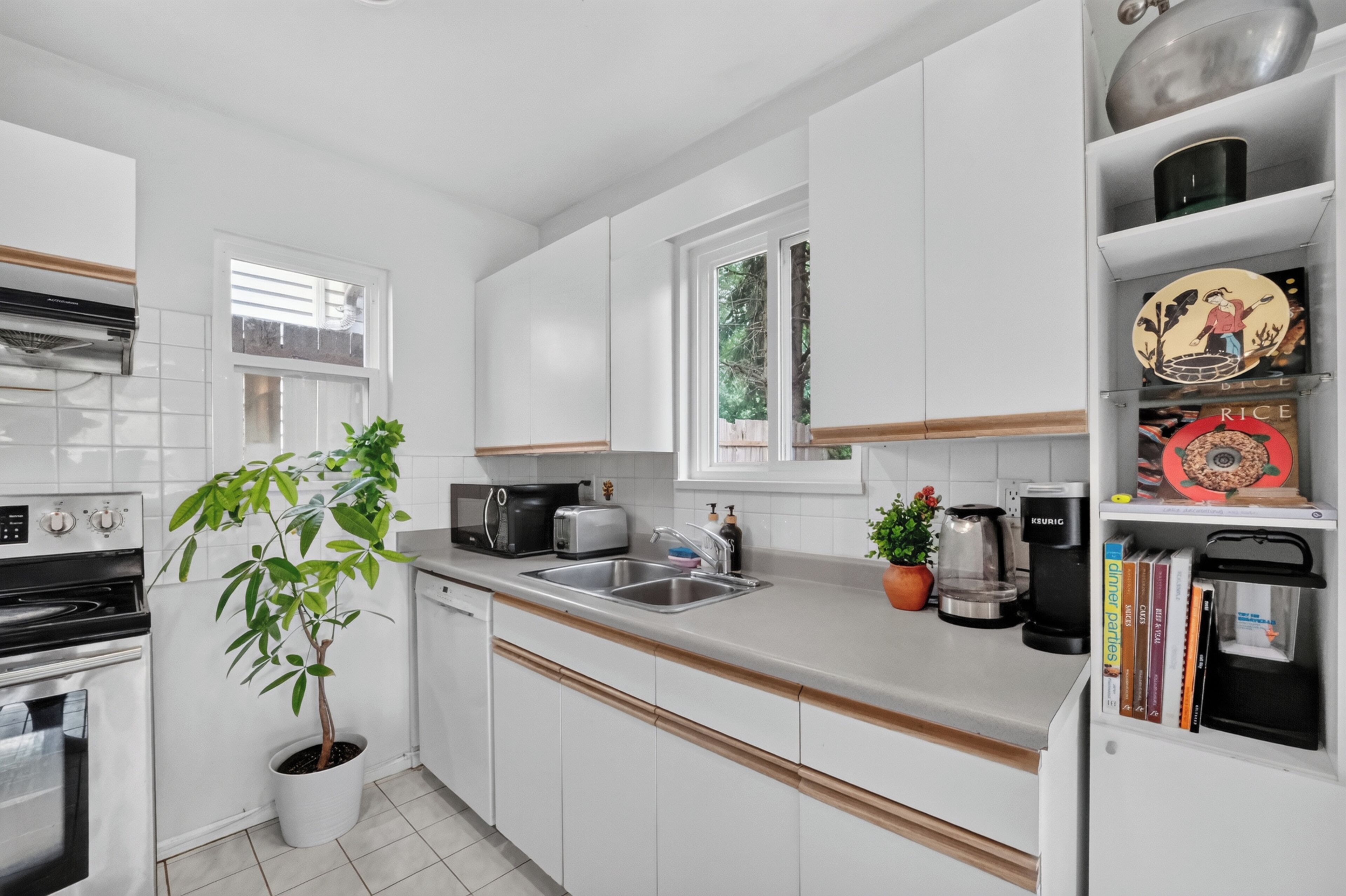 Una cocina moderna con armarios blancos, horno empotrado, microondas, cafetera y una planta en maceta.