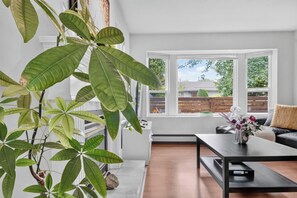 En moderne stue med et stort vindue, et sofabord, en sofa og en potteplante.