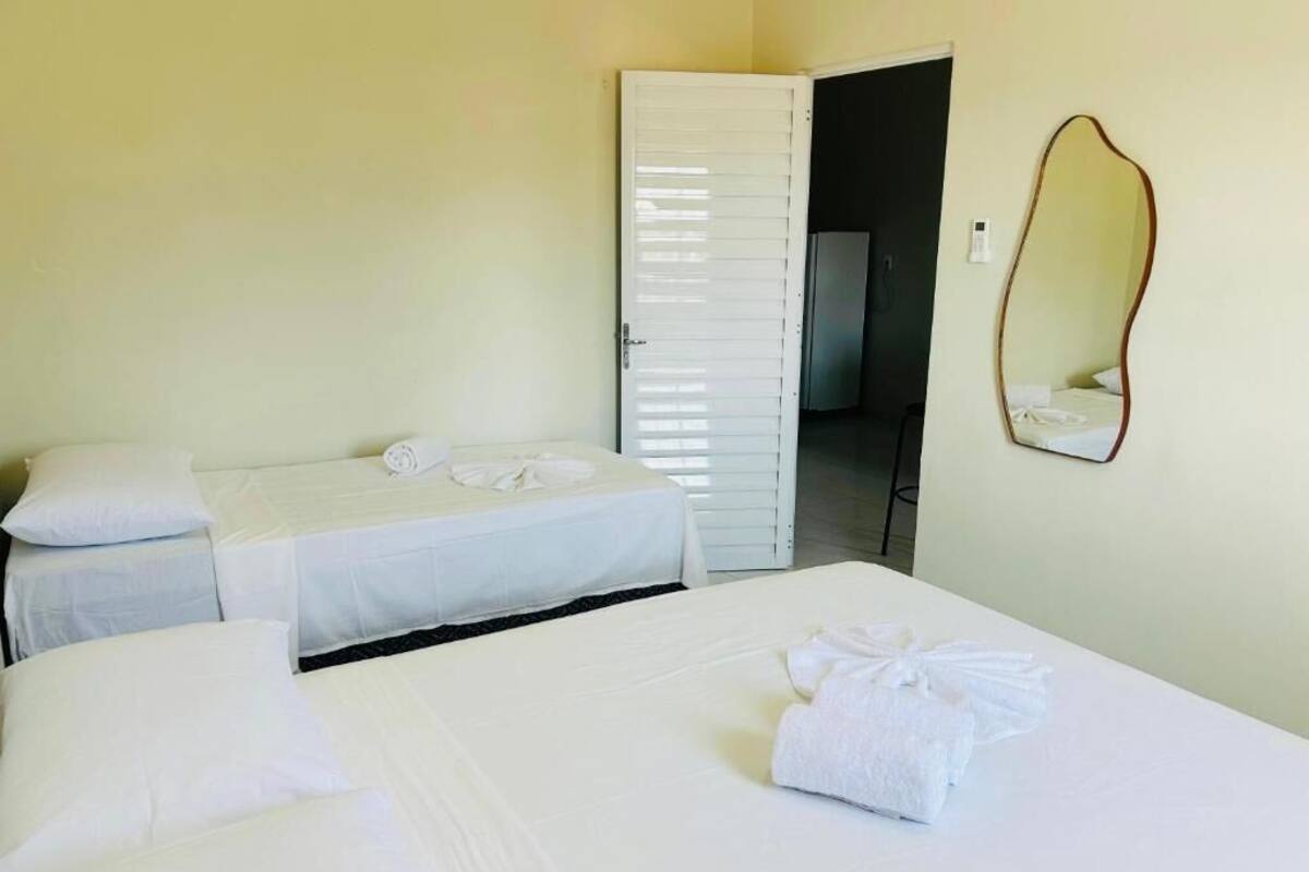 Una habitación de hotel con dos camas individuales, una cama grande, un espejo y una puerta que da a un baño.