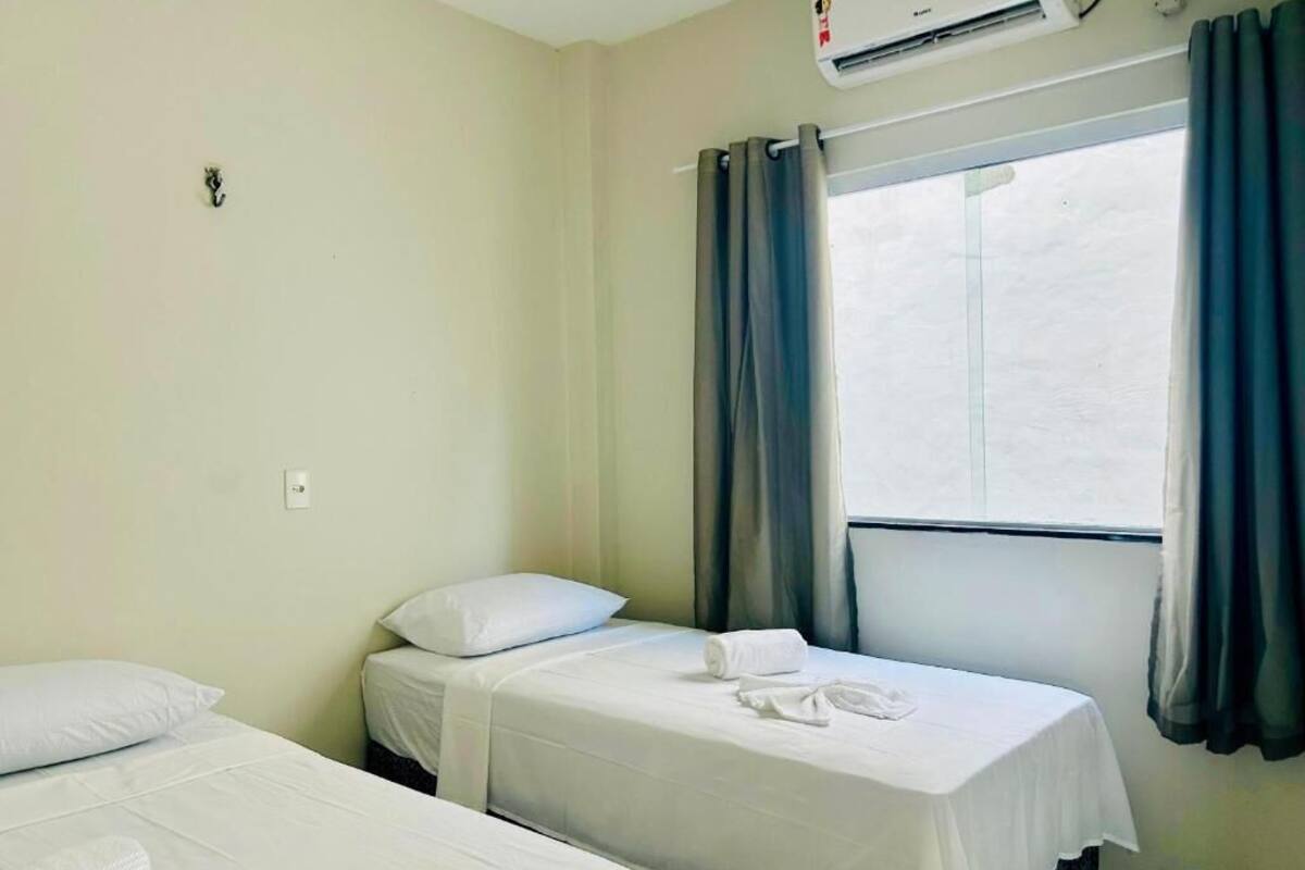 Habitación de hotel con dos camas, una ventana con cortinas, un aire acondicionado y un interruptor de luz en la pared.