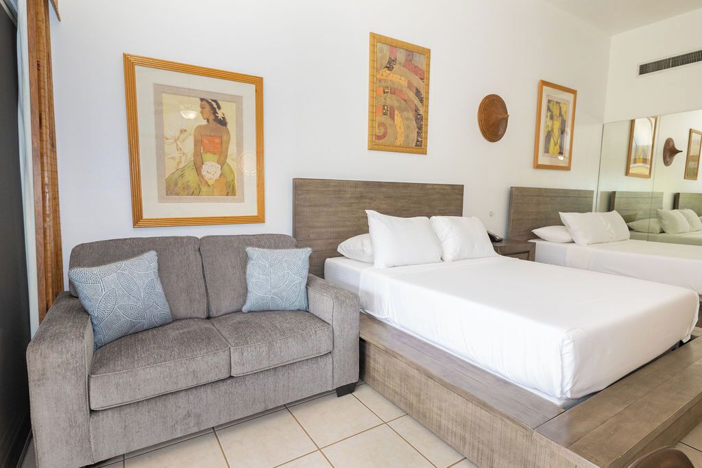 A hotel room with a sofa, two beds, and framed artwork on the walls.