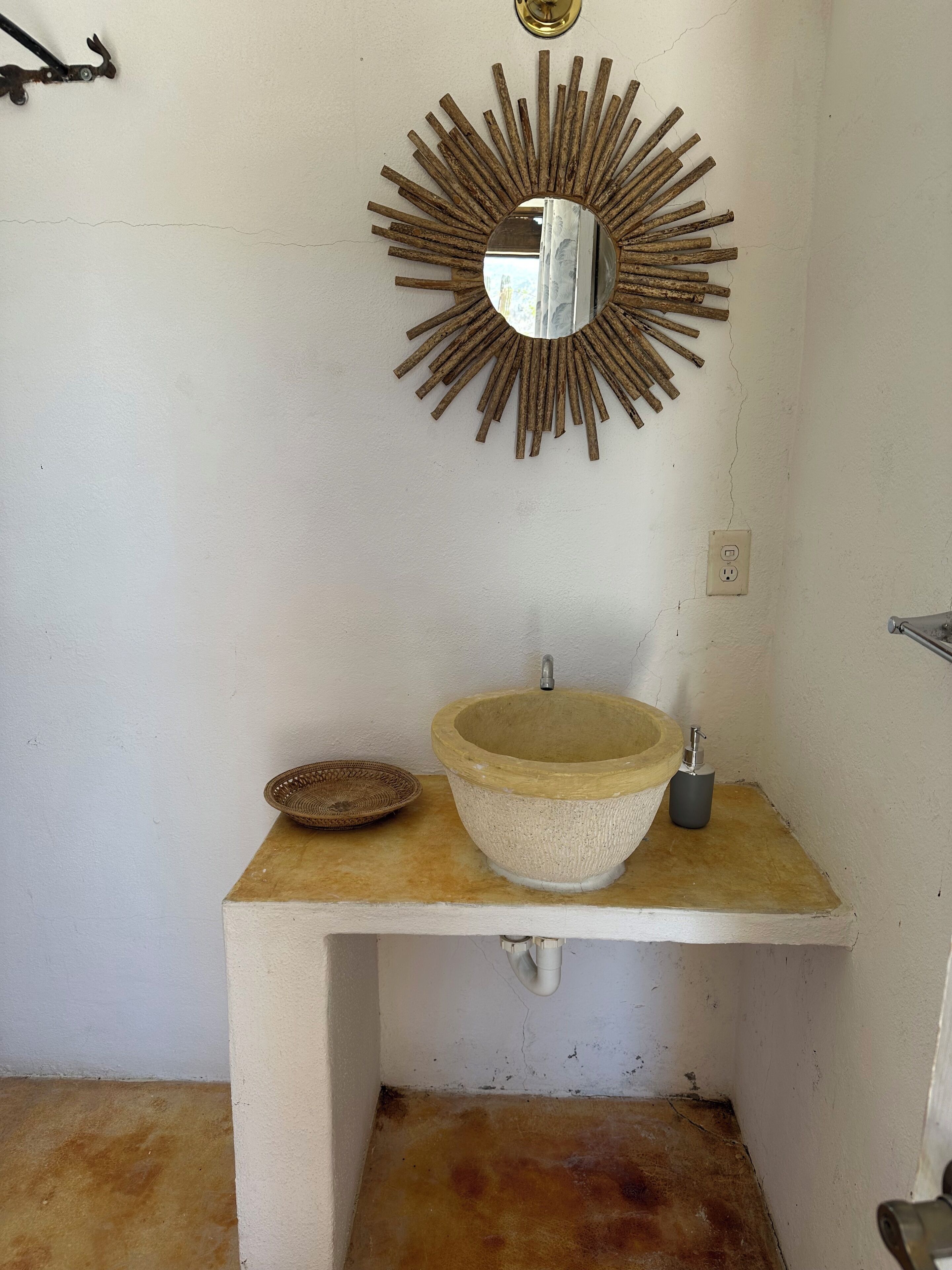 A bathroom with a sunburst mirror, a stone sink, a small woven basket, and a faucet.