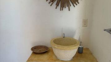 A bathroom with a sunburst mirror, a stone sink, a small woven basket, and a faucet.