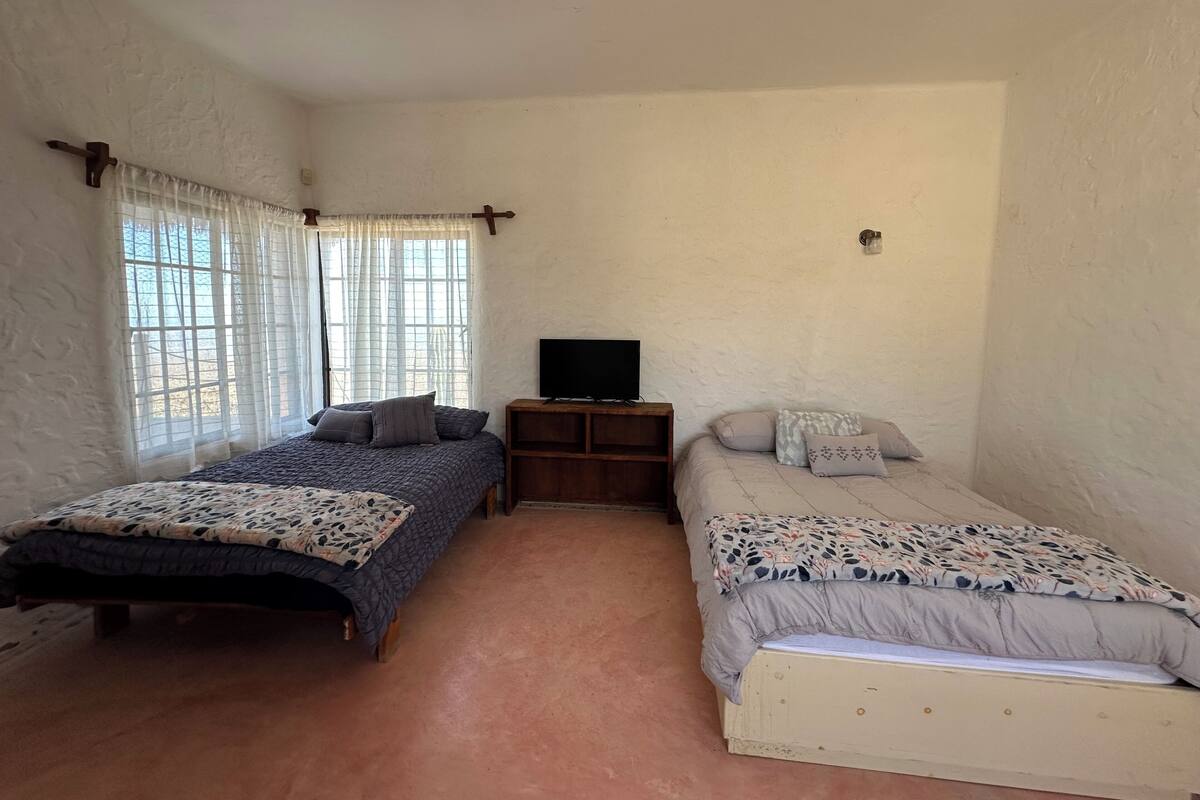 A bedroom with two beds, a TV stand, and a window with curtains.