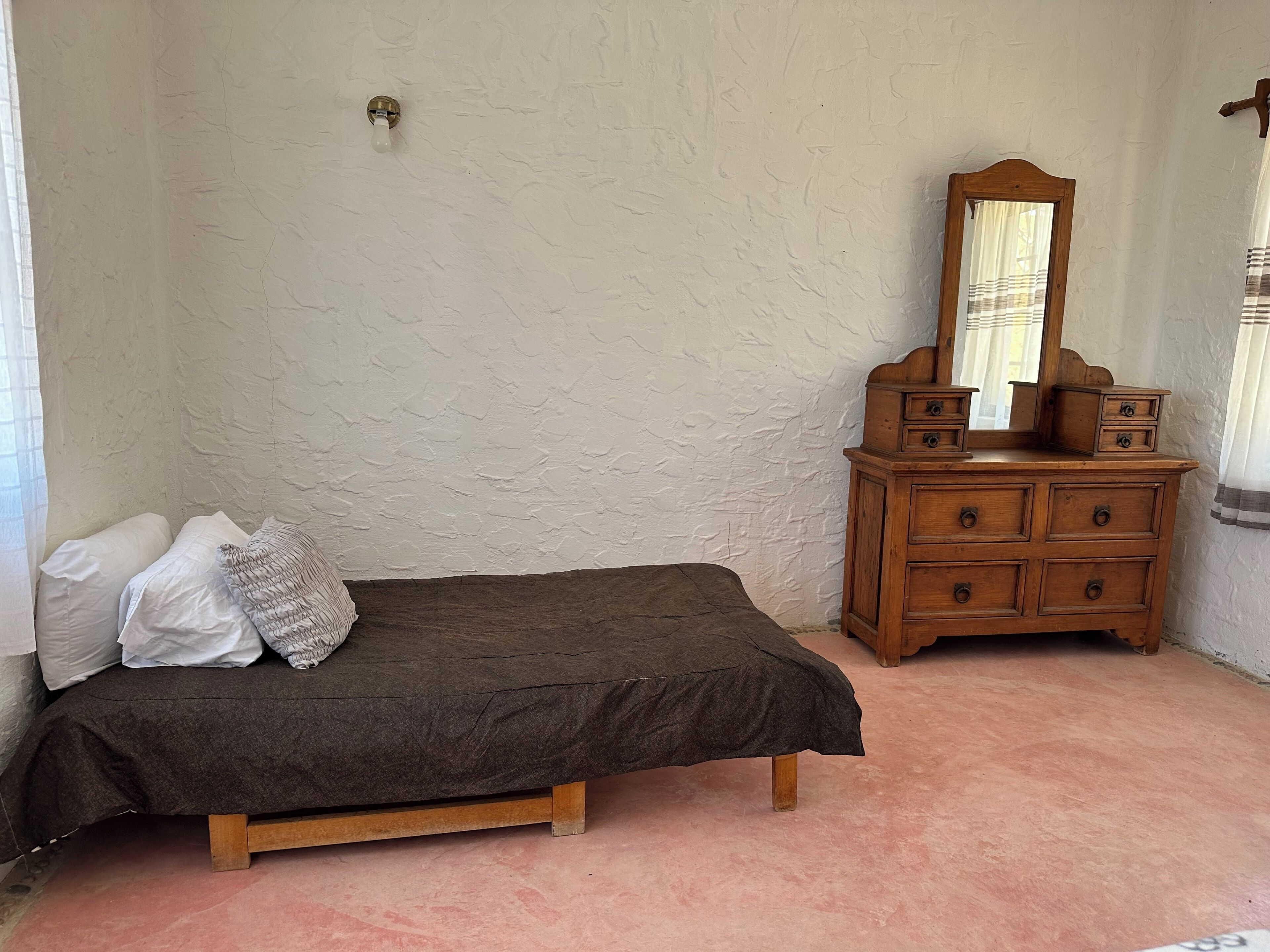 Ein Schlafzimmer mit einem Einzelbett, einer Holzkommode mit Schubladen, einem Spiegel und einer Wandleuchte.