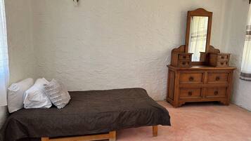 Ein Schlafzimmer mit einem Einzelbett, einer Holzkommode mit Schubladen, einem Spiegel und einer Wandleuchte.