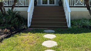 Una casa a due piani con un portico, una scalinata che conduce all'ingresso e un giardino con palme.