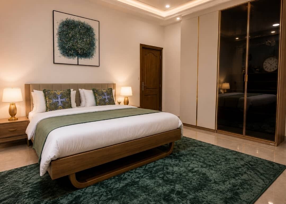 Une chambre à coucher moderne avec un grand lit, un tapis vert, une tête de lit en bois, une œuvre d’art accrochée au mur et un placard avec une porte coulissante en verre.
