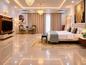 Una habitación de hotel moderna con una cama grande, televisión, candelabro y una obra de arte de gran tamaño en la pared.